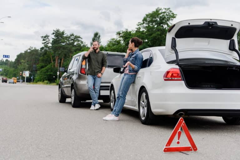 Image is of two drivers standing near vehicles after a car accident in Aiken, with a warning triangle placed on the road to indicate a rear end collision scene