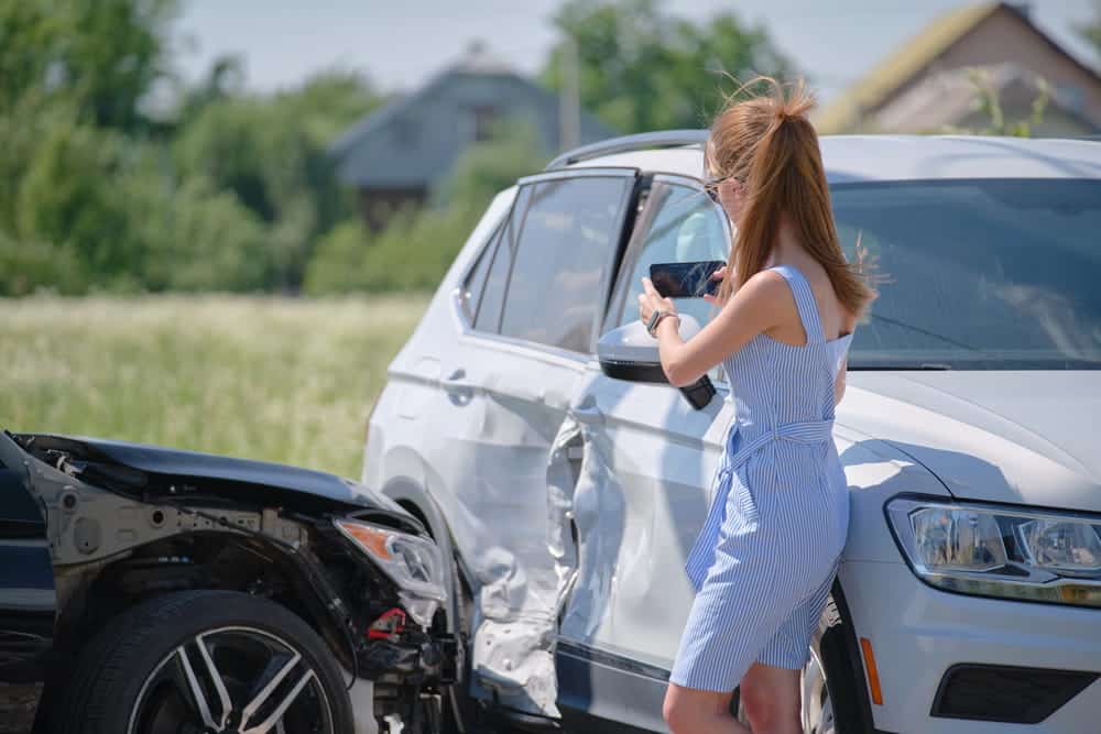 Image is of a woman taking photos of vehicle damage after a car accident in Aiken, showing the process of documenting evidence at the crash scene