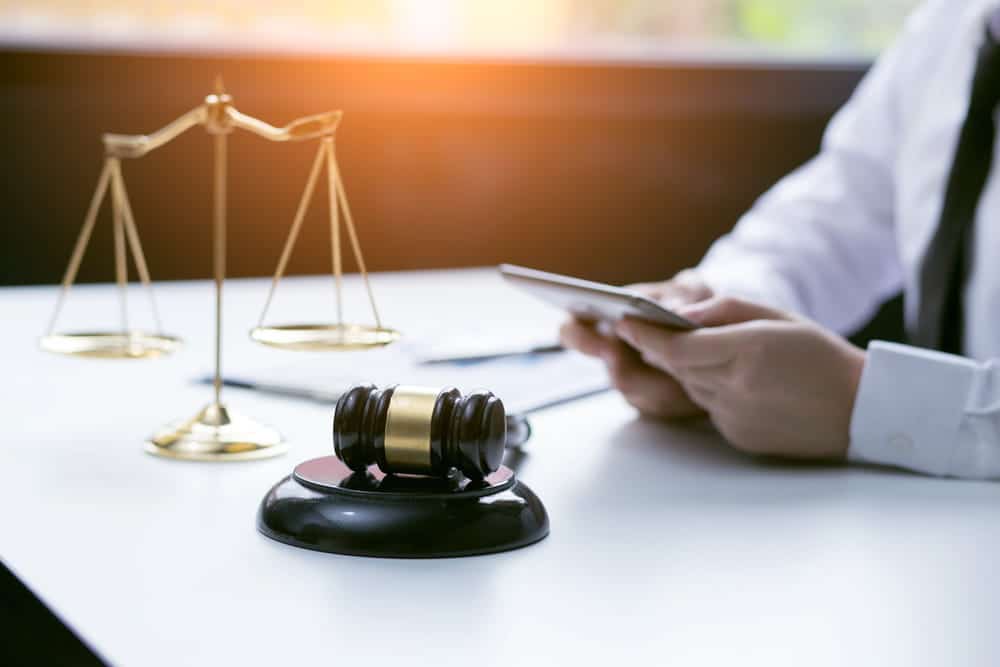 Image is of a legal professional holding a phone near a gavel and scales, concept of reviewing digital communication in DV cases in Aiken