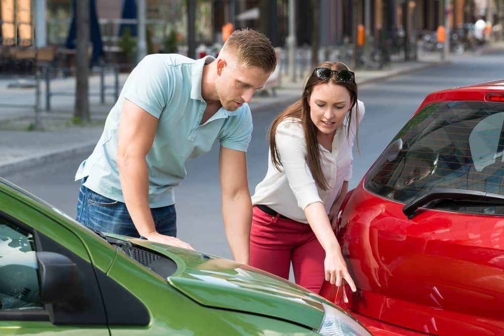 Image is of two drivers inspecting car damage on the street after a crash, illustrating evidence review in an Aiken car accident