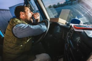 Image is of a truck driver yawning while driving inside a cabin, showing fatigue as a cause of truck accidents in Aiken