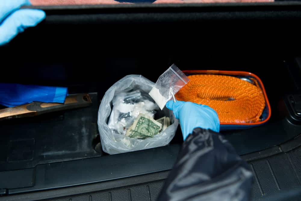 Image is of a gloved officer holding a small bag of suspected drugs found in a vehicle trunk, showing how evidence supports drug possession in Aiken cases