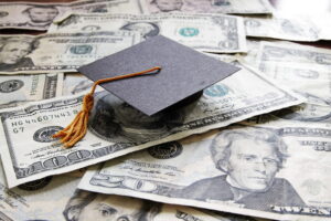 Image is of a graduation cap placed across scattered cash, concept of drug charges affecting college funding and federal student aid access.