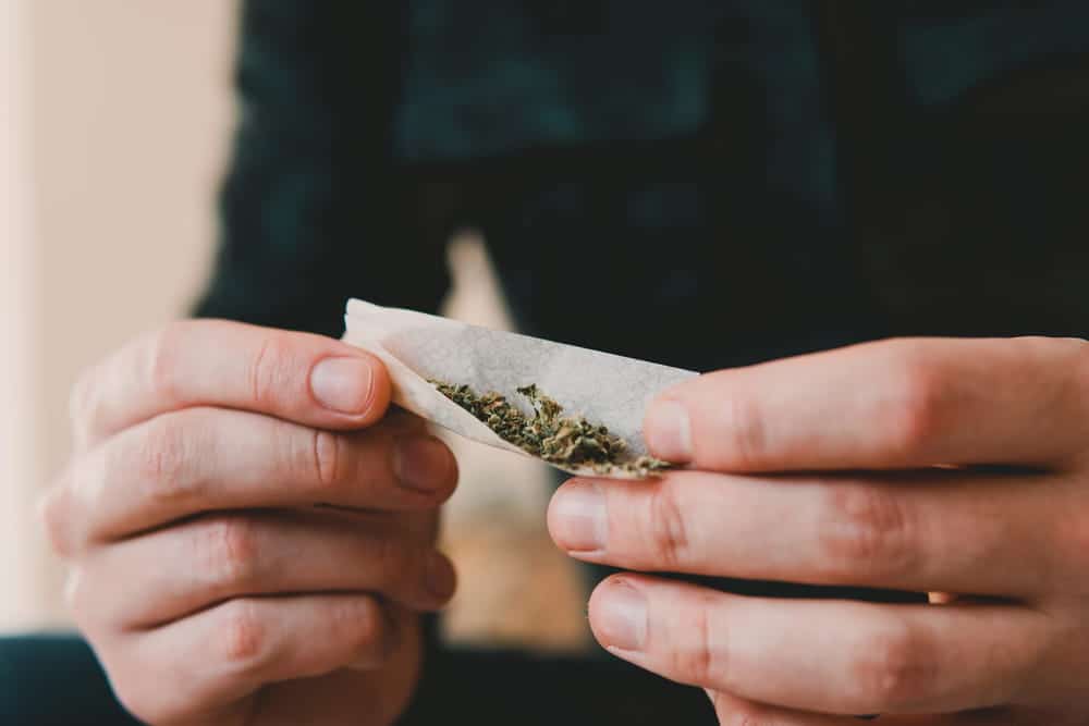 Image is of a person holding and rolling marijuana by hand, concept of drug charges connected to student financial aid concerns.