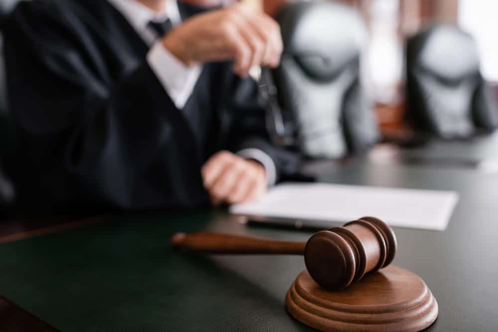 Image is of a courtroom gavel with lawyers seated in the background, concept of legal proceedings connected to DV charges in Aiken.