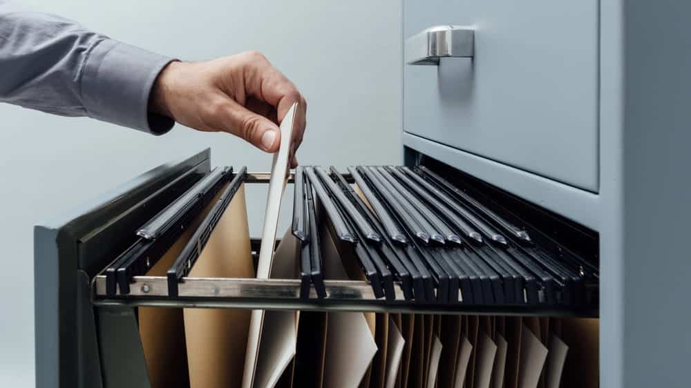 Image is of a hand placing files inside a records cabinet, concept of DV charges stored in criminal record systems in Aiken.