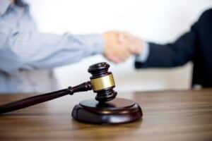Image is of a legal handshake with a gavel on the table, concept of motorcycle accident settlement negotiations after an Aiken crash.