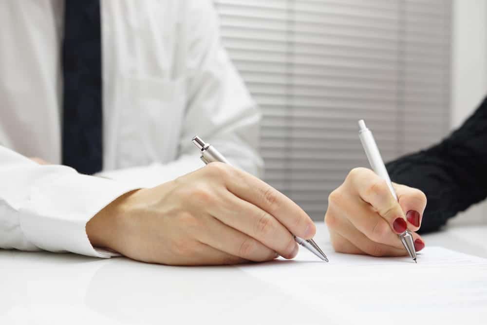Image is of two people signing legal documents, concept of motorcycle accident settlement paperwork and claim review.