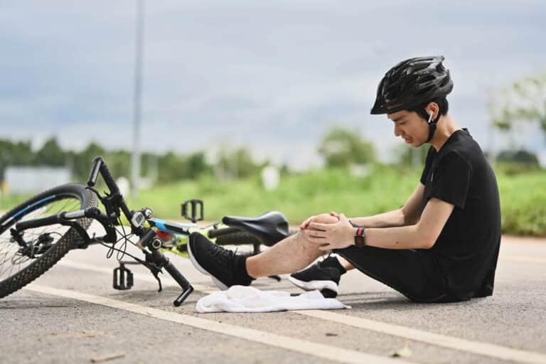 Image is of an injured cyclist sitting beside a bicycle on the roadside, concept of seeking medical attention after a bike accident in Aiken.