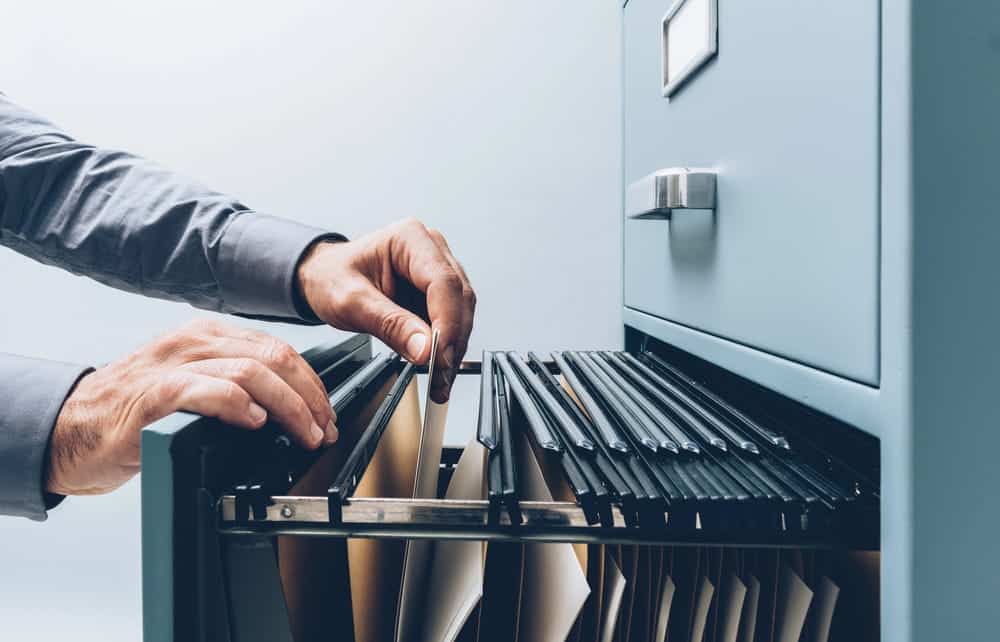 Image is of a person searching through physical document files, concept of archived DUI records and background check investigations in Aiken.