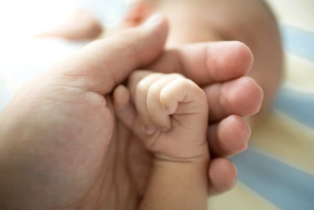 mage is of an adult holding a newborn baby's hand, concept of an Aiken adoption lawyer helping families establish a permanent legal parent child relationship.
