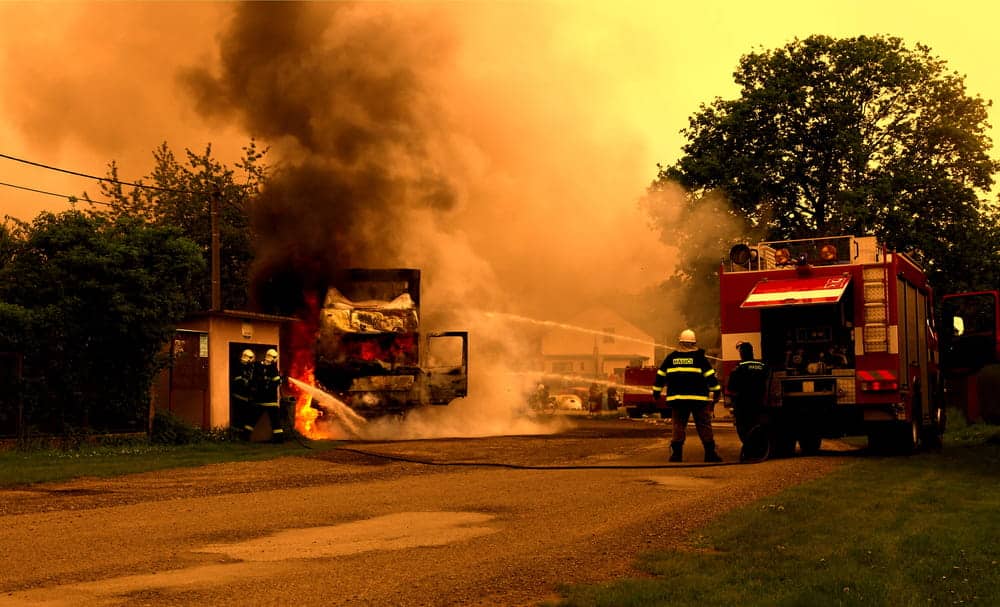 Image is of firefighters responding to a vehicle fire with heavy smoke, concept of an Aiken arson lawyer defending clients facing fire-related criminal allegations.