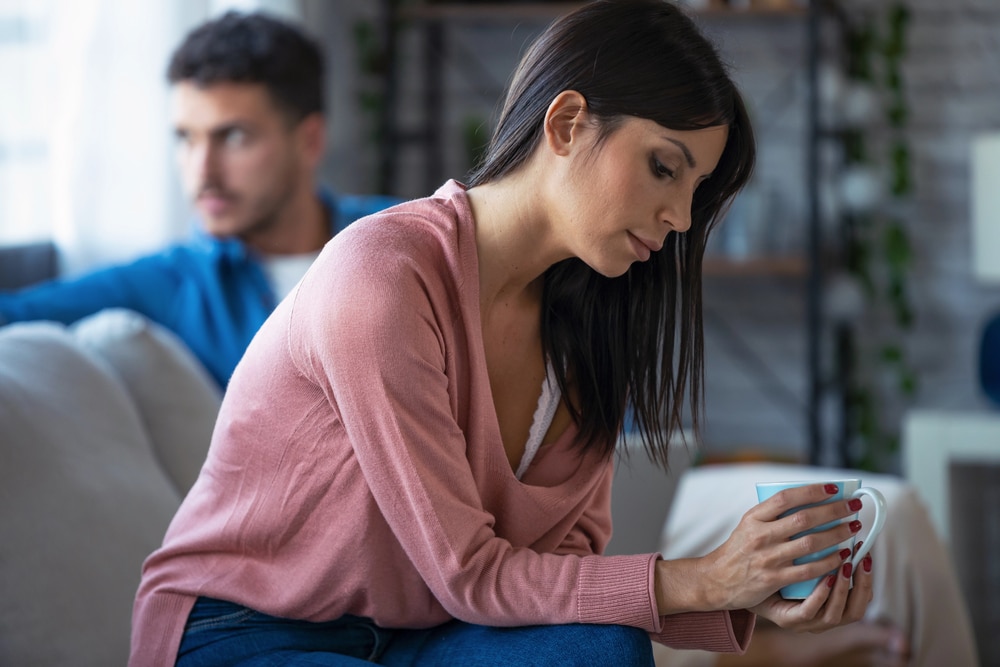Image is of an individual appearing distressed while seated with another person in the background, concept of an assault and battery lawyer assisting clients facing serious criminal allegations.