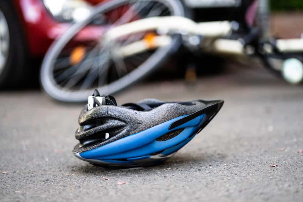 Image is of a bicycle helmet in the foreground with injured cyclists after a crash, concept of a bicycle accident lawyer helping victims after a serious collision.