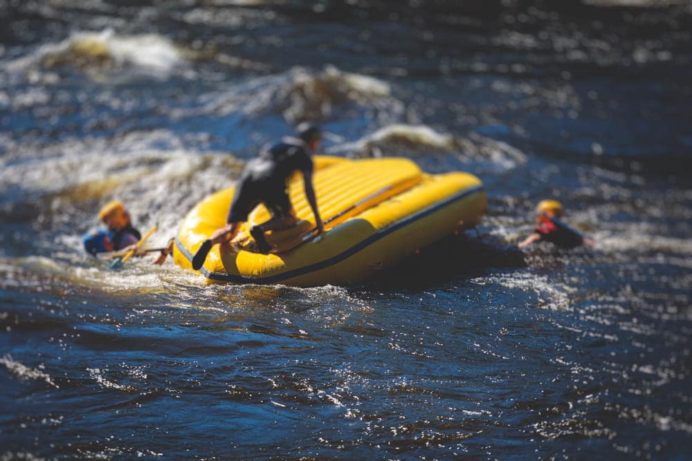 Image is of people attempting to recover after an inflatable raft overturns in rough water, concept of a boating accident lawyer assisting injured victims after a recreational watercraft accident.