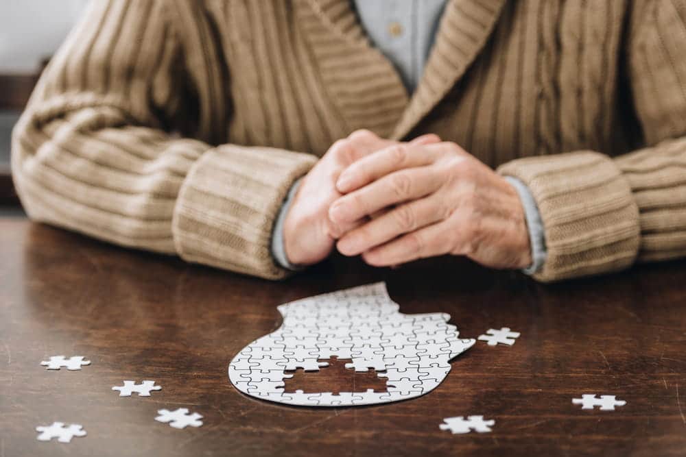 Image is of a person sitting beside a brain-shaped puzzle with missing pieces, concept of an Aiken brain injury lawyer addressing cognitive and neurological injury claims.