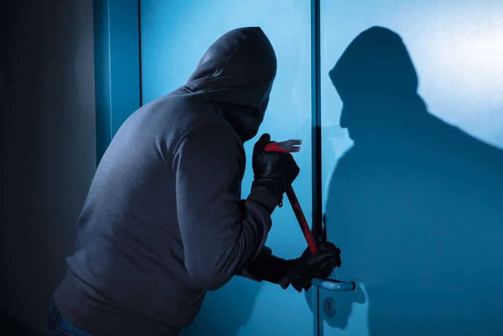 Image is of an individual attempting to force entry through a door, concept of an Aiken burglary lawyer handling allegations involving unlawful entry into a structure.
