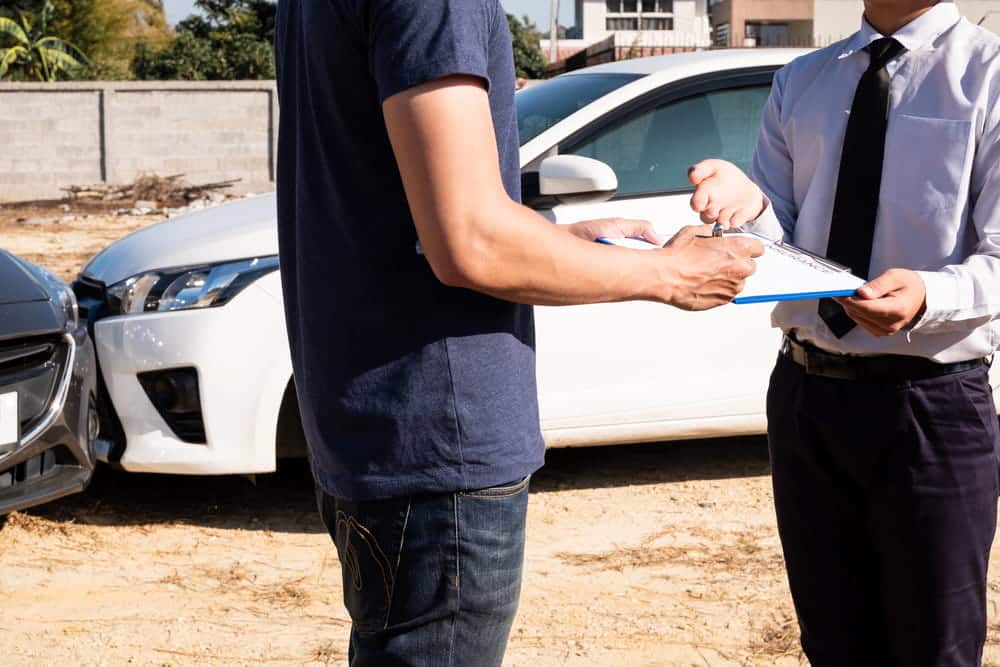 Image is of an individual providing information and completing paperwork following a vehicle collision, concept of a car accident attorney.
