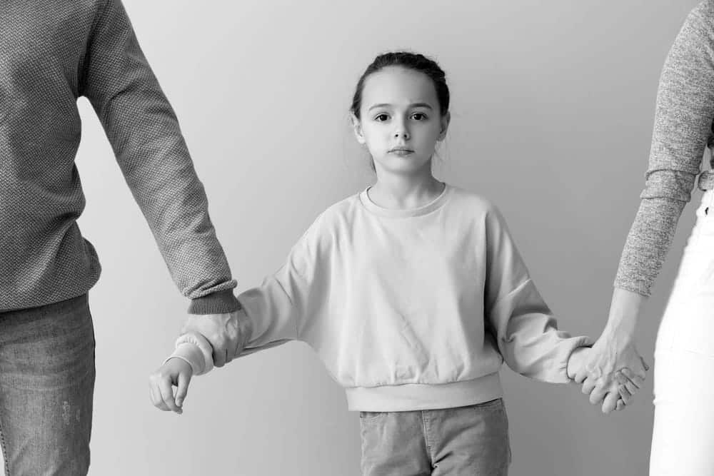 Image is of a child standing between separated parents, concept of custody concerns discussed with a contested divorce lawyer in Aiken.