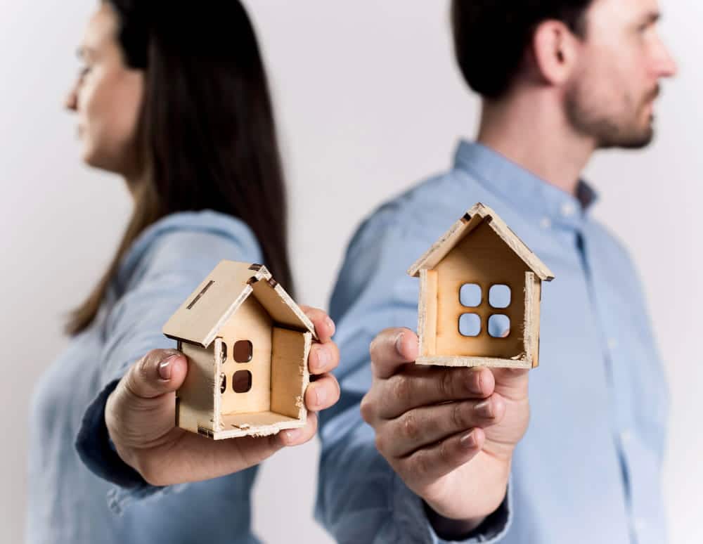 Image is of a separated couple holding individual house models, concept of property division issues handled by a contested divorce lawyer in Aiken.