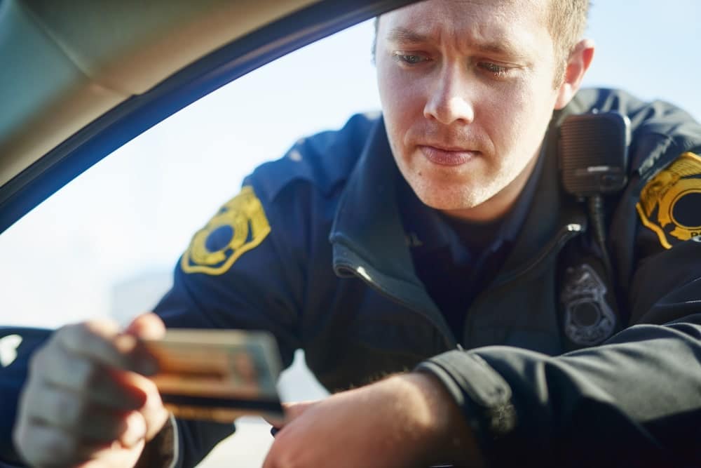 Image is of a law enforcement officer reviewing a driver's identification during a traffic stop, concept of a DUI license suspension lawyer assisting after a DUI arrest.
