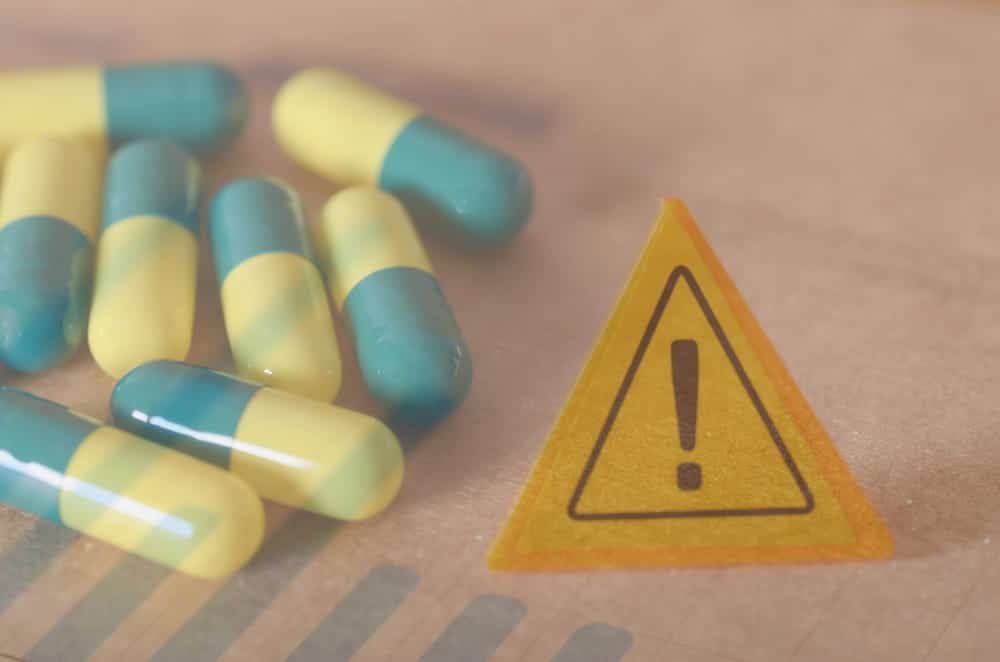 Image is of prescription capsules beside a medical warning symbol, concept of an Aiken defective drugs lawyer handling claims involving dangerous medications.