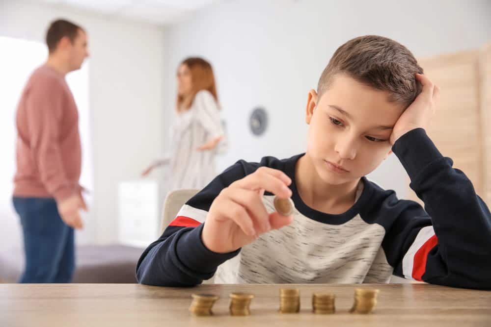 Image is of a child counting coins while parents argue in the background, concept of a divorce with children lawyer addressing child support and family financial concerns.