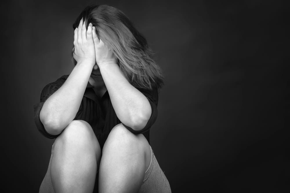 Image is of an individual sitting with their face covered in apparent emotional distress, concept of a domestic violence lawyer helping clients address the legal and personal challenges associated with domestic violence allegations.