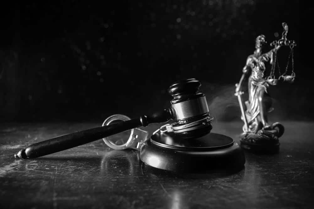 Image is of a judge's gavel, handcuffs, and a Lady Justice statue on a desk, concept of a domestic violence lawyer handling criminal defense matters related to domestic violence charges.