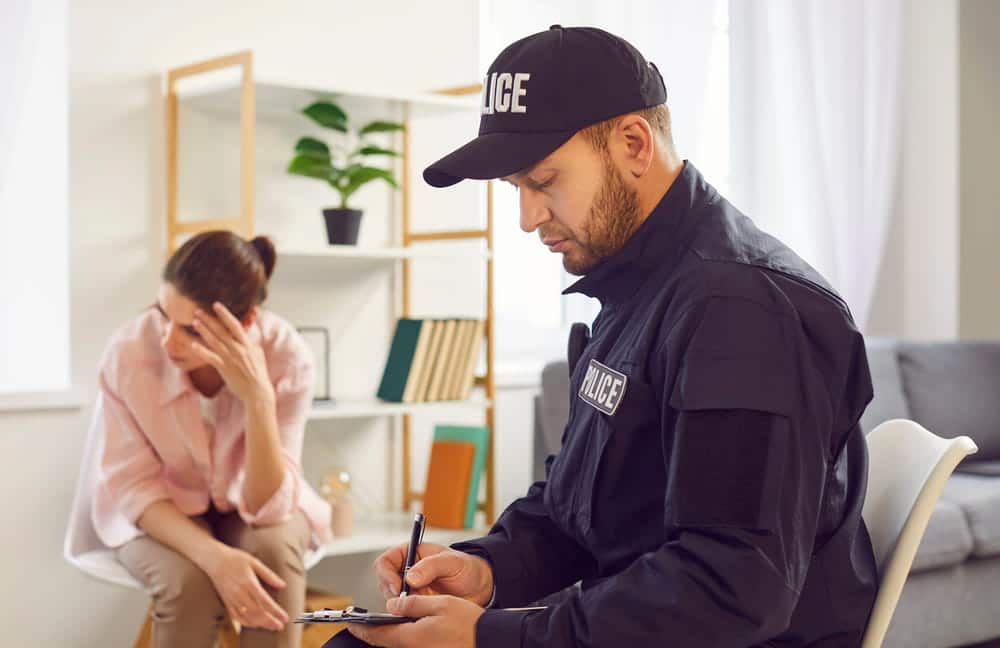 Image is of a police officer taking notes while speaking with an individual who appears distressed, concept of a domestic violence lawyer assisting clients during a domestic violence investigation.