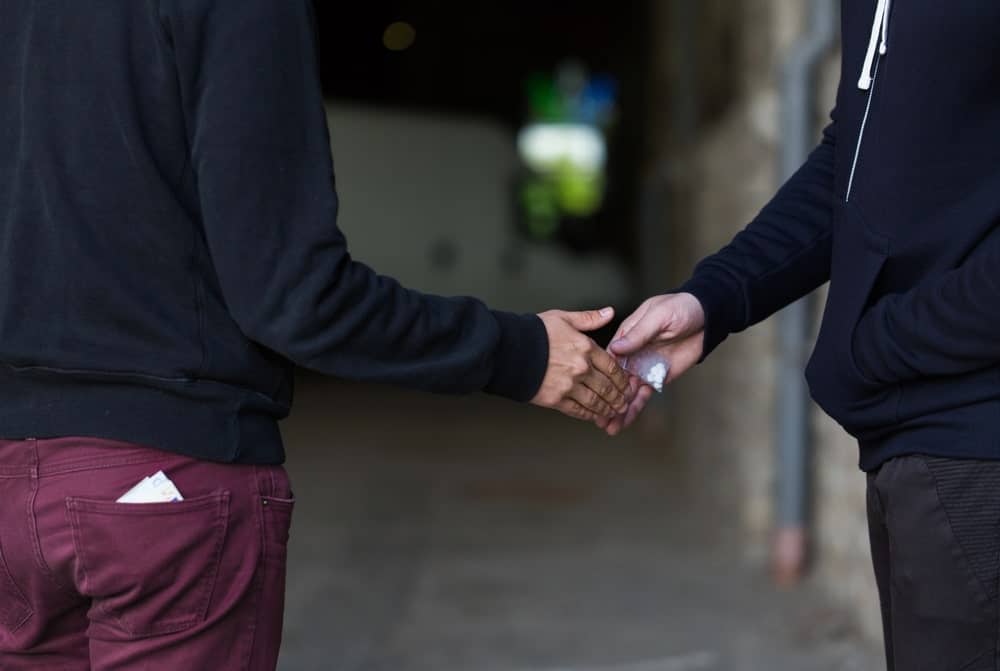 Image is of a small packet being exchanged between individuals, concept of an Aiken drug distribution lawyer examining evidence related to alleged drug transactions.