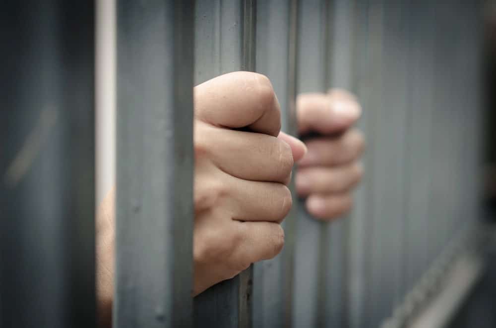 Image is of a person gripping jail cell bars, concept of an Aiken drug manufacturing lawyer protecting the rights of someone facing serious criminal charges.
