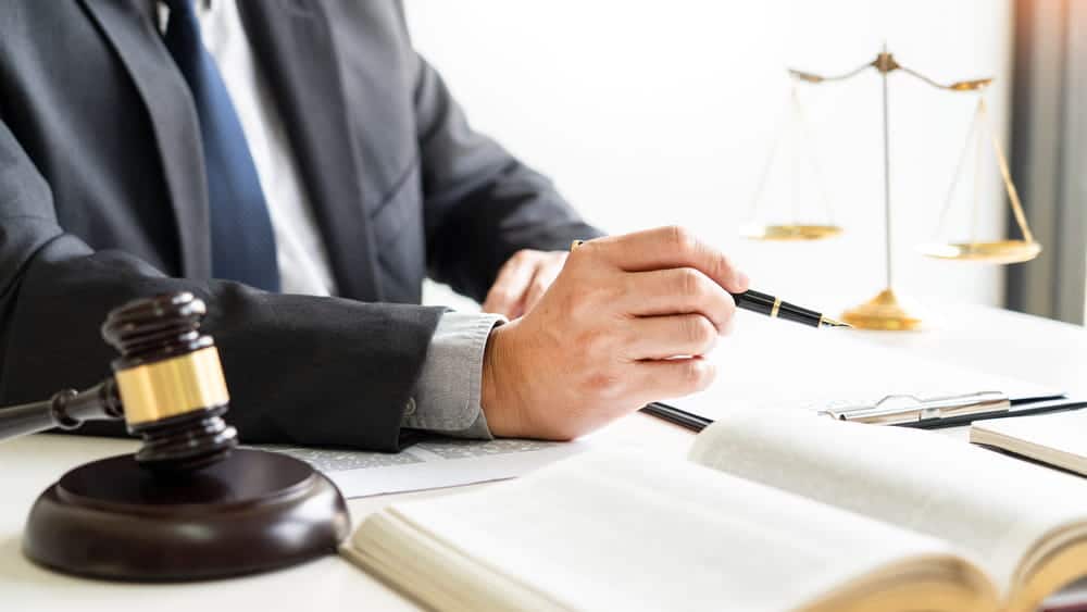 Image is of an attorney reviewing legal documents with a gavel and scales of justice, concept of an Aiken drug trafficking lawyer evaluating defense strategies in a criminal case.