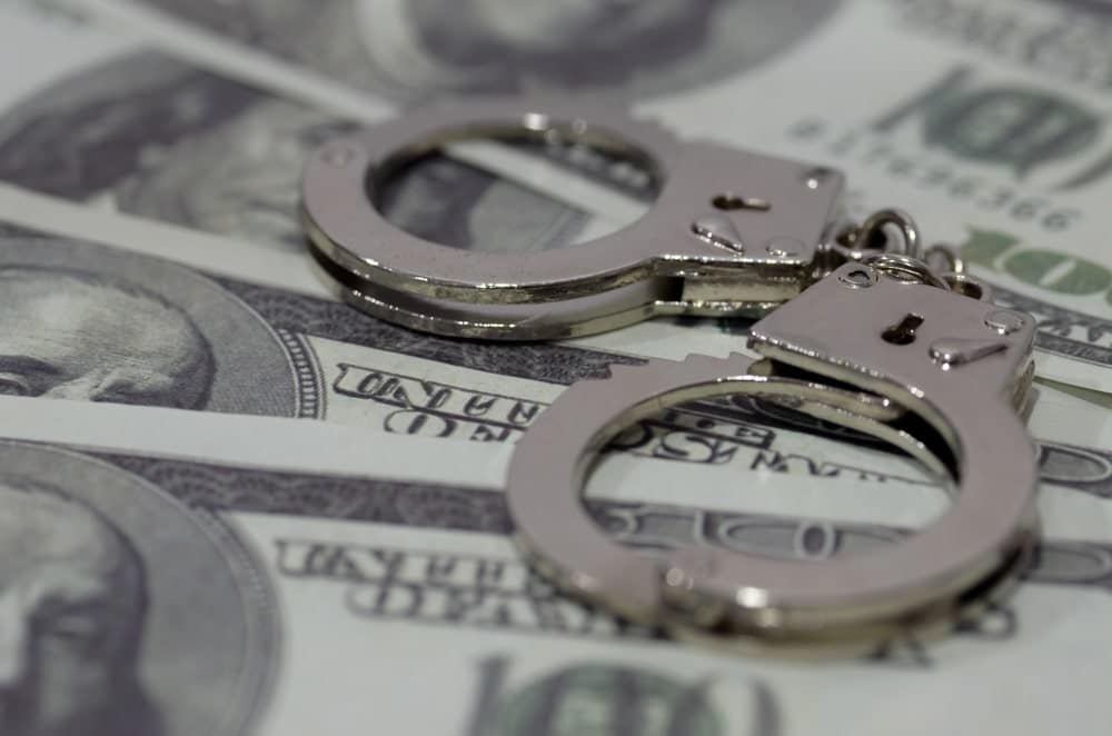 Image is of handcuffs placed on currency, concept of an Aiken drug trafficking lawyer addressing allegations involving financial evidence and controlled substances.