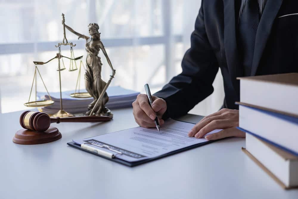 Image is of an attorney reviewing and signing legal documents near a gavel and scales of justice, concept of a first offense DUI lawyer preparing a defense strategy for DUI allegations.