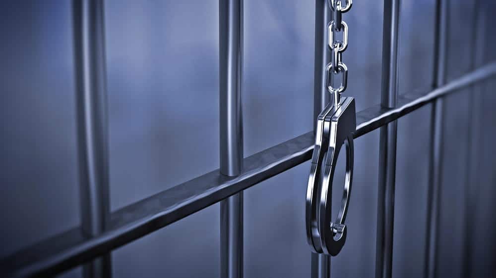 Image is of handcuffs hanging from jail cell bars, concept of an Aiken insider trading lawyer defending clients facing federal criminal charges.