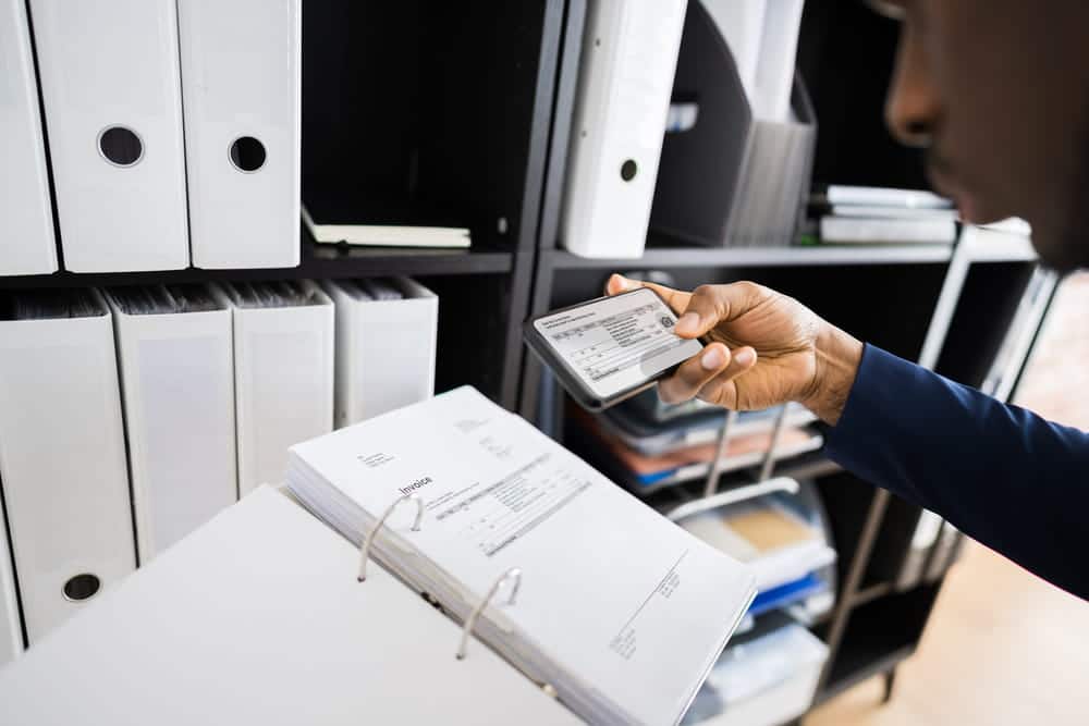 Image is of a person reviewing business records on a mobile device beside office files, concept of an Aiken intellectual property theft lawyer analyzing company document evidence.