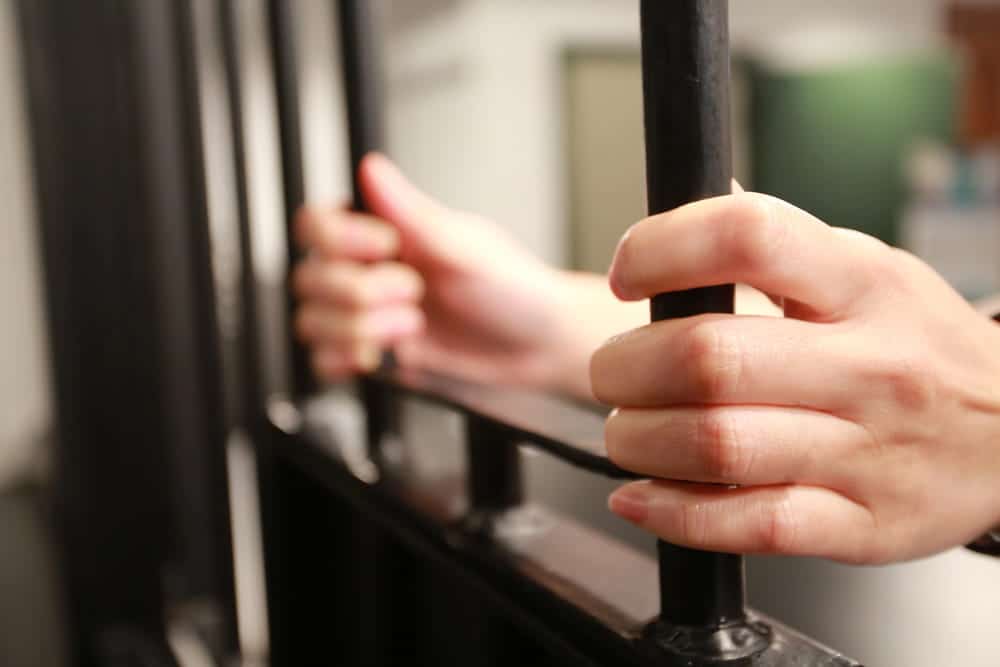 Image is of hands gripping jail cell bars, concept of an Aiken intellectual property theft lawyer defending clients facing criminal charges.