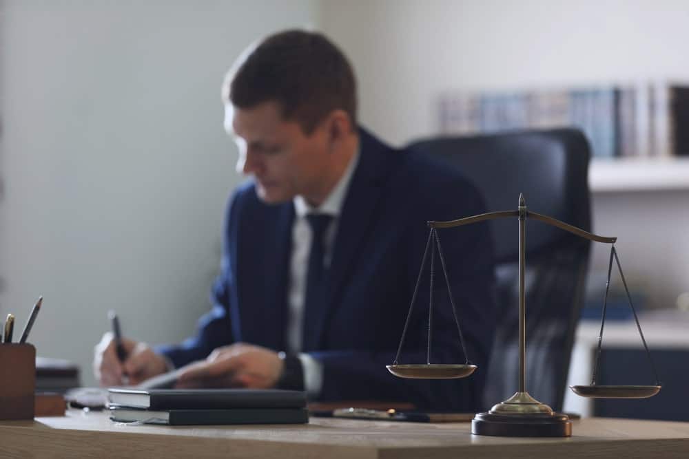 Image is of a lawyer working at a desk with the scales of justice in the foreground, concept of an Aiken intellectual property theft lawyer preparing a criminal defense case.