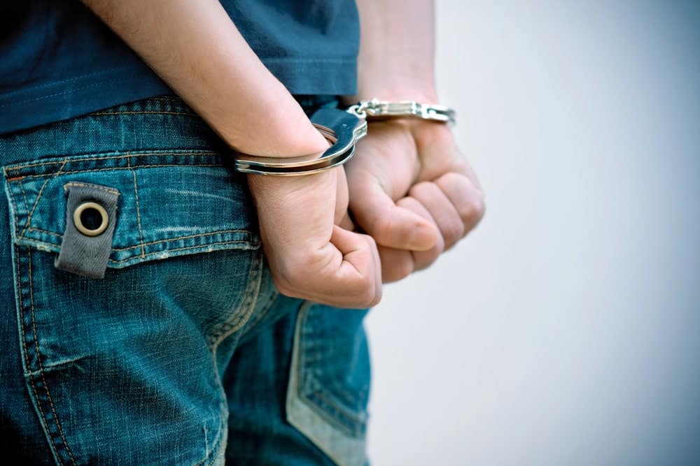 Image is of a teenager wearing handcuffs behind their back, concept of a juvenile criminal defense lawyer protecting a young person's legal rights after an arrest.