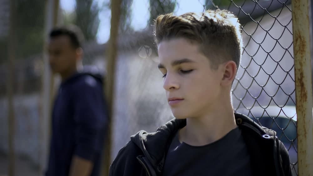 Image is of a concerned teenager standing near a fence, concept of a juvenile criminal defense lawyer assisting minors facing criminal allegations and court involvement.
