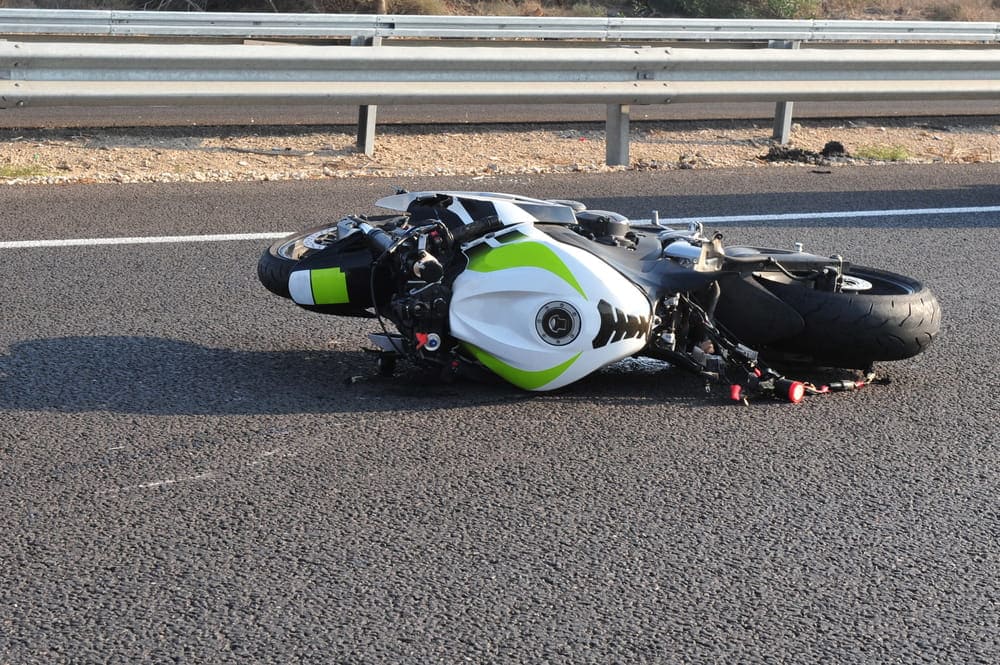 Image is of a motorcycle lying on the roadway after a collision, concept of a motorcycle accident lawyer investigating crash causes and liability.