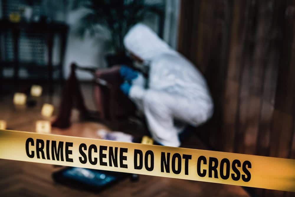 Image is of a crime scene investigator collecting evidence behind police tape, concept of an Aiken murder defense lawyer examining investigative findings and evidence.