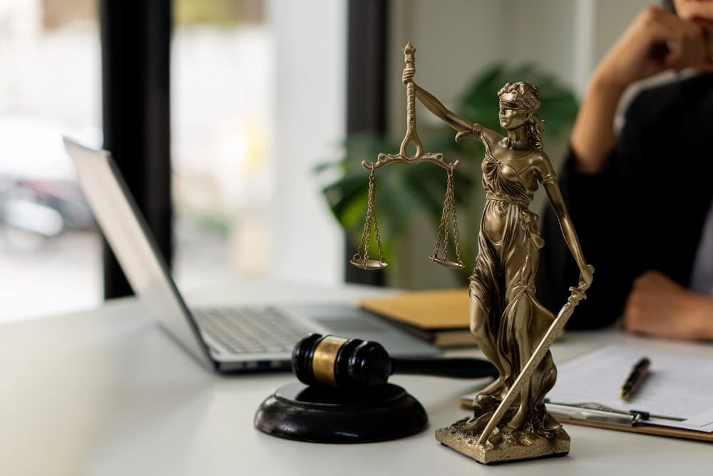 Image is of a Lady Justice statue beside a laptop and legal workspace, concept of an Aiken name change lawyer preparing and reviewing court documents for a name change petition.