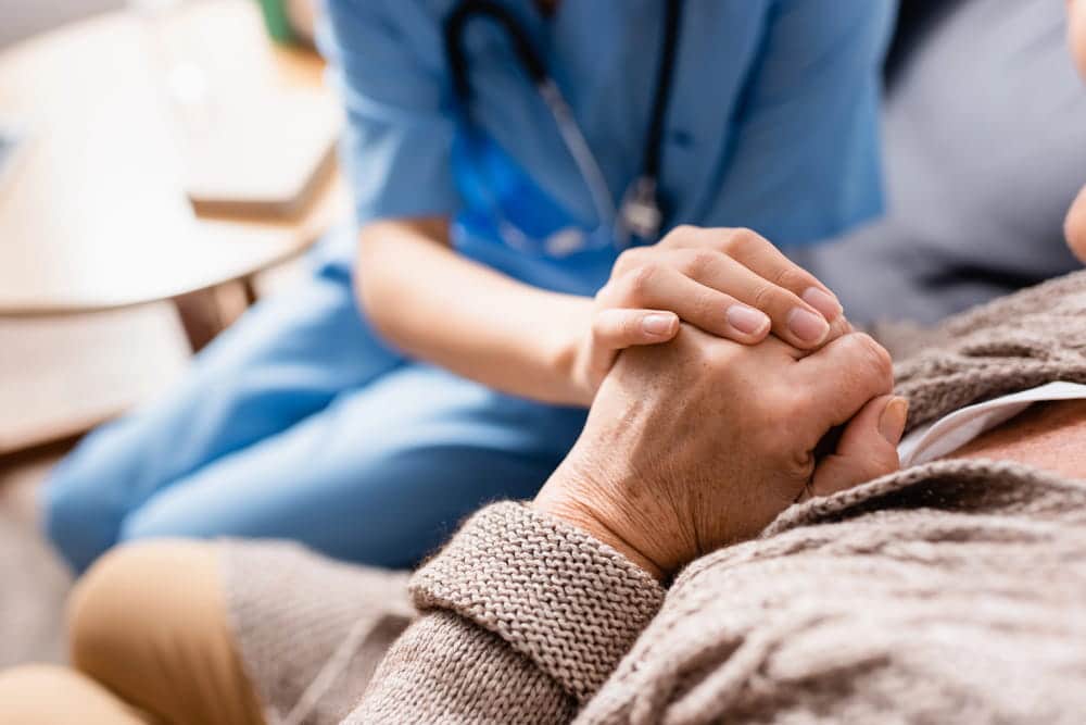 Image is of a healthcare worker comforting an elderly patient by holding their hand, concept of an Aiken nursing home abuse and neglect lawyer helping families protect vulnerable loved ones.