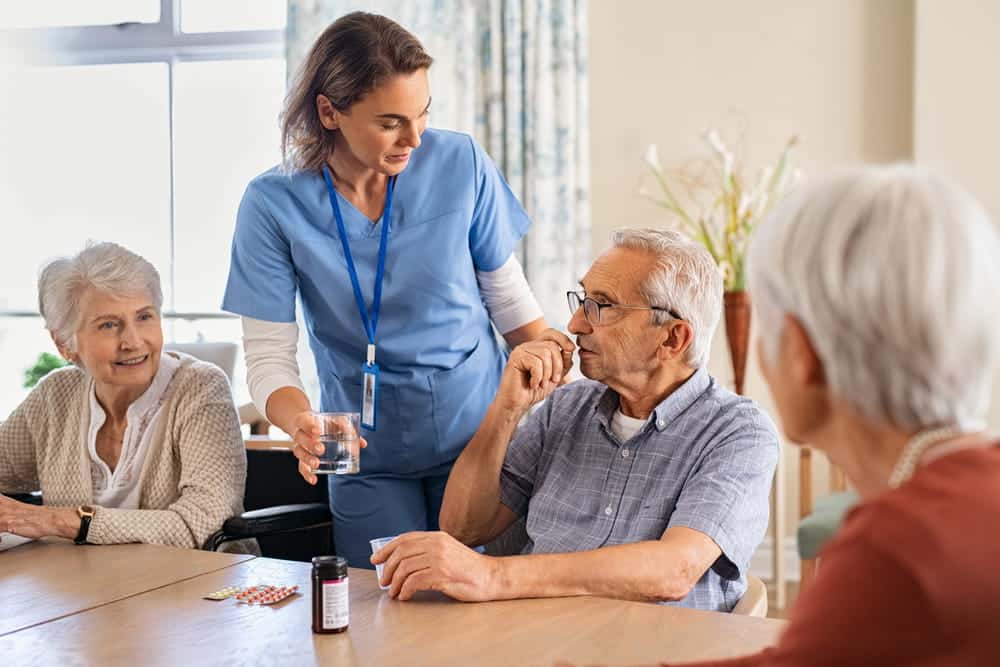Image is of a caregiver assisting nursing home residents with medication and daily care, concept of an Aiken nursing home abuse and neglect lawyer addressing concerns about resident safety.