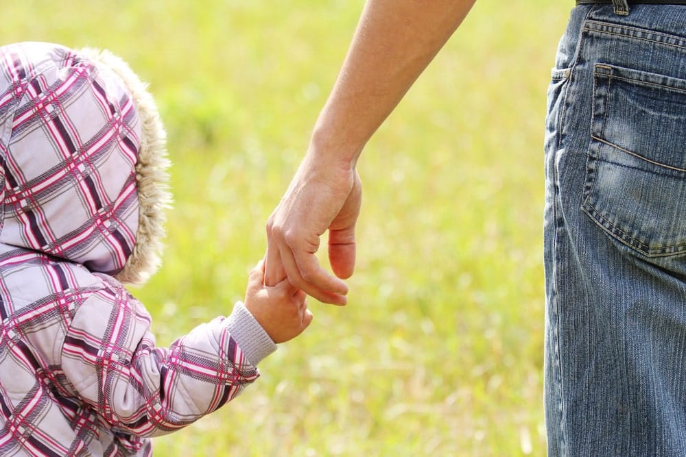 Image is of an adult holding a young child's hand outdoors, concept of an Aiken paternity lawyer helping establish legal parental rights and responsibilities.