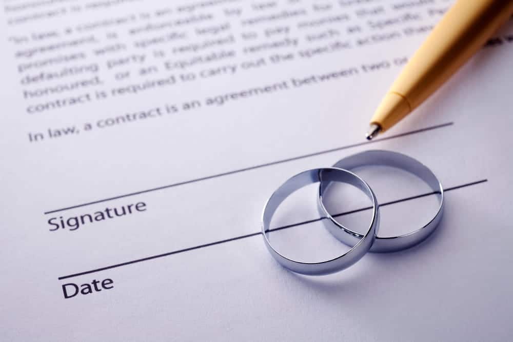 Image is of wedding rings resting on a signed legal agreement, concept of an Aiken postnuptial agreement lawyer helping married couples formalize financial arrangements after marriage.