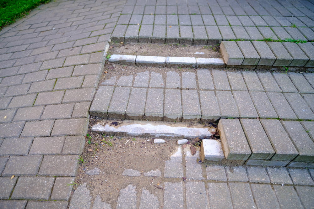Image is of uneven and damaged pavement creating a tripping hazard, concept of a premises liability lawyer helping injured victims recover compensation for unsafe property conditions.