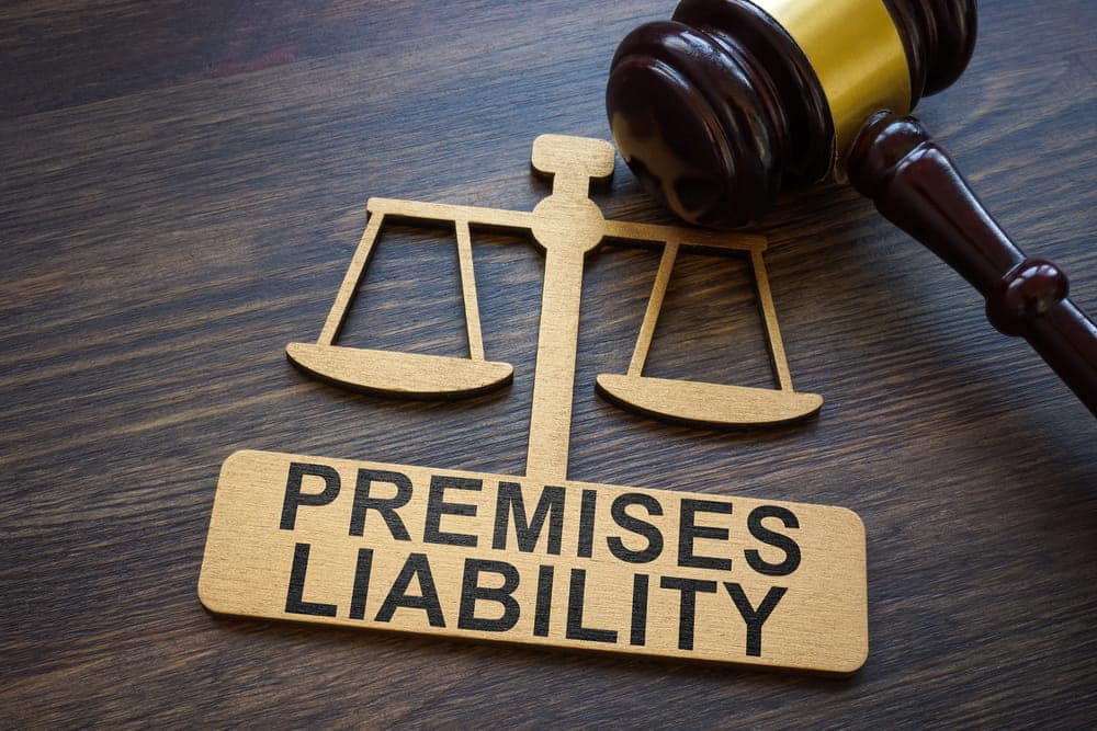 Image is of a judge's gavel and scales with a premises liability sign, concept of a premises liability lawyer helping injured visitors pursue compensation for unsafe property conditions.
